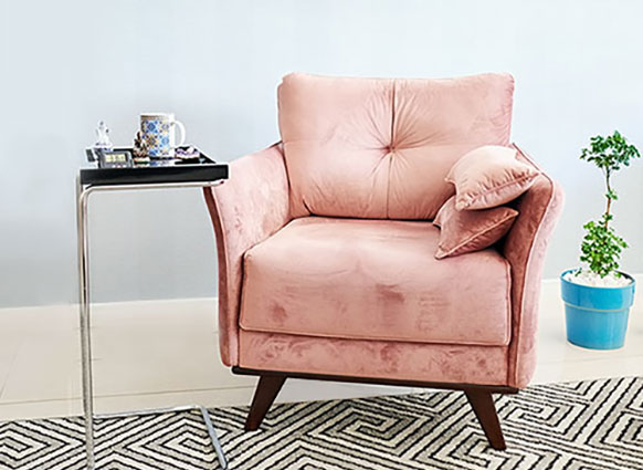 Rosa fåtölj med brunt sidobord och en blå kruka med krukväxt i på golvet